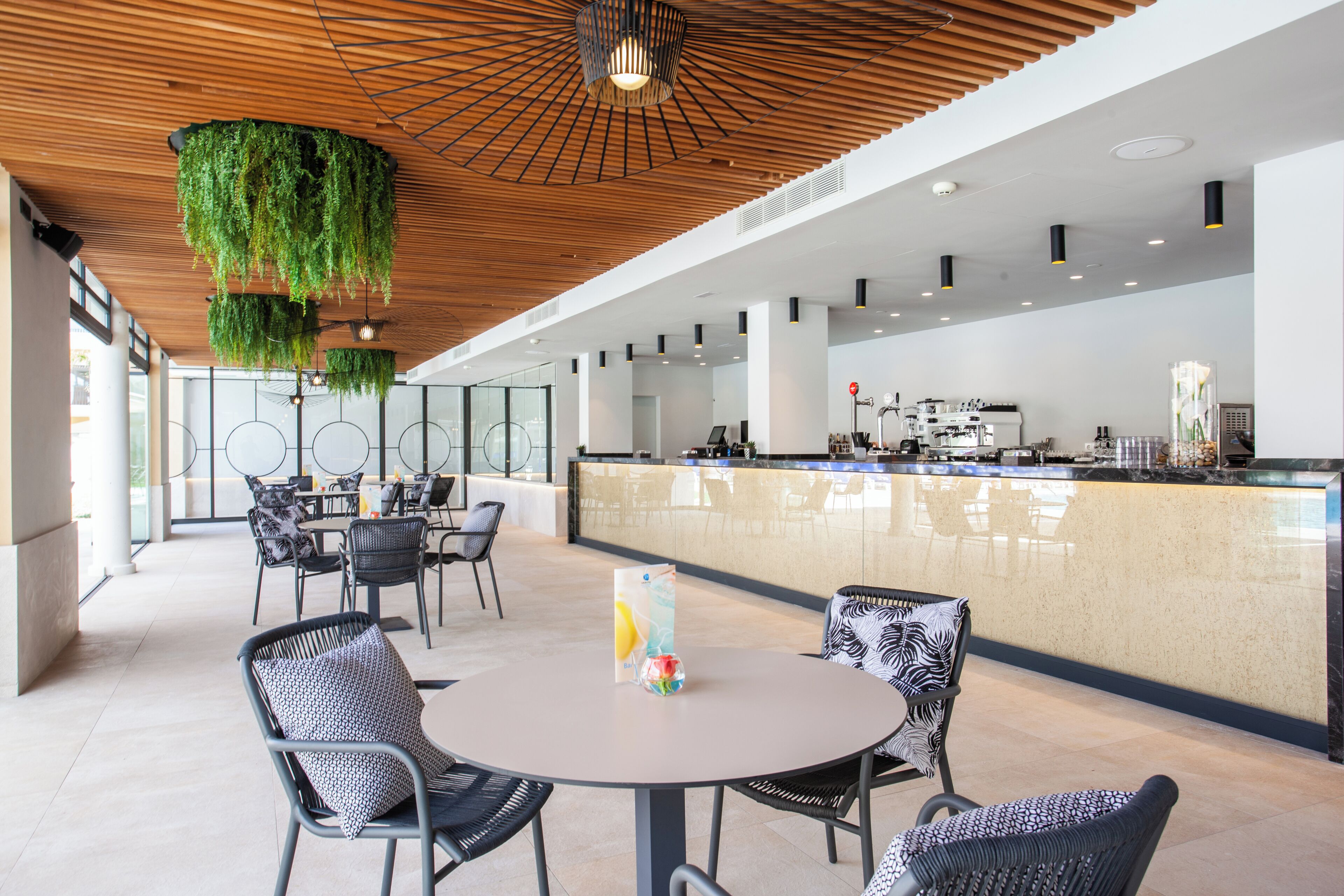 Un espacio interior moderno con techo de madera, una zona de bar y diferentes disposiciones de asientos.