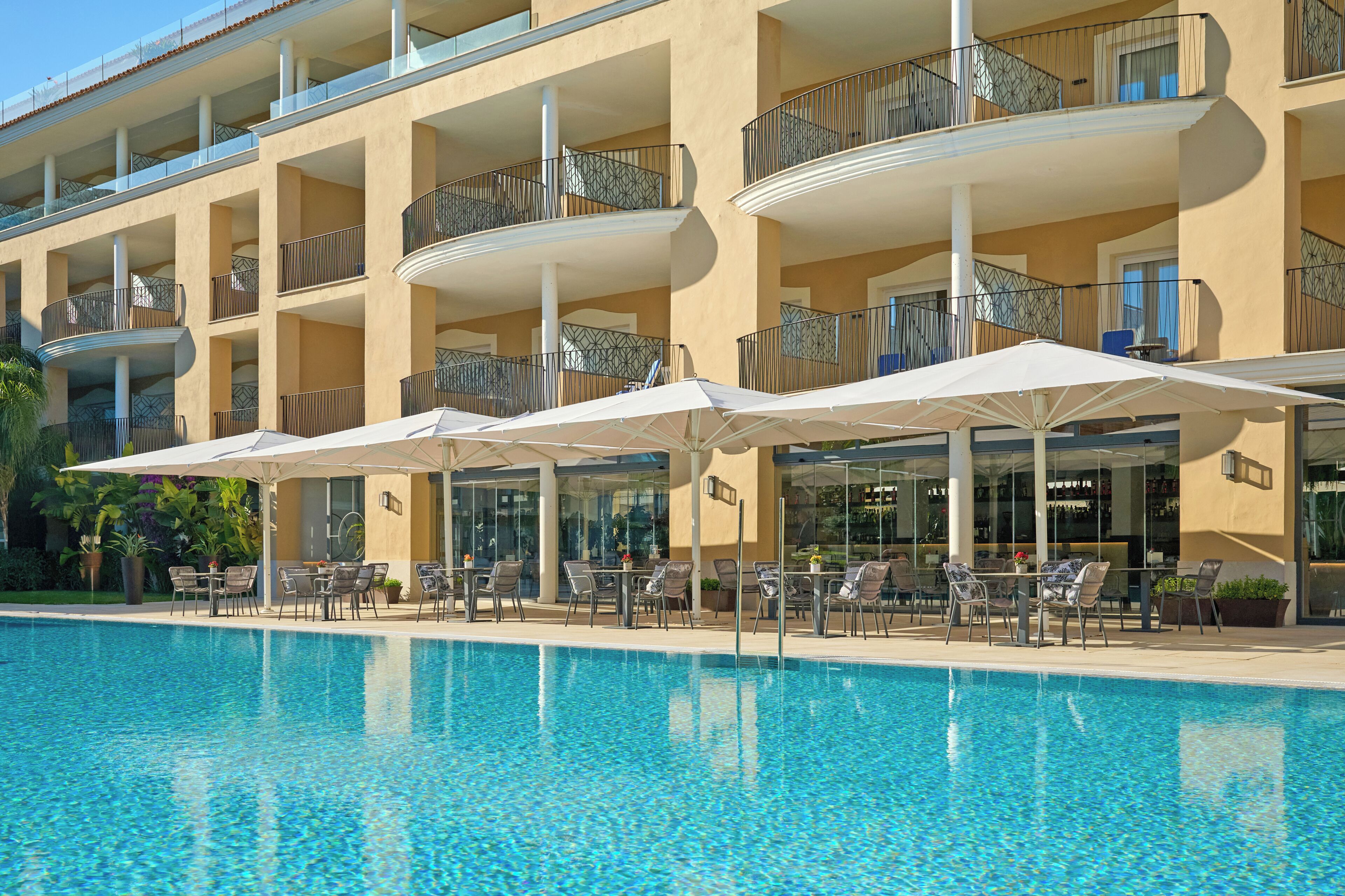 A hotel with a swimming pool, outdoor seating, and balconies.
