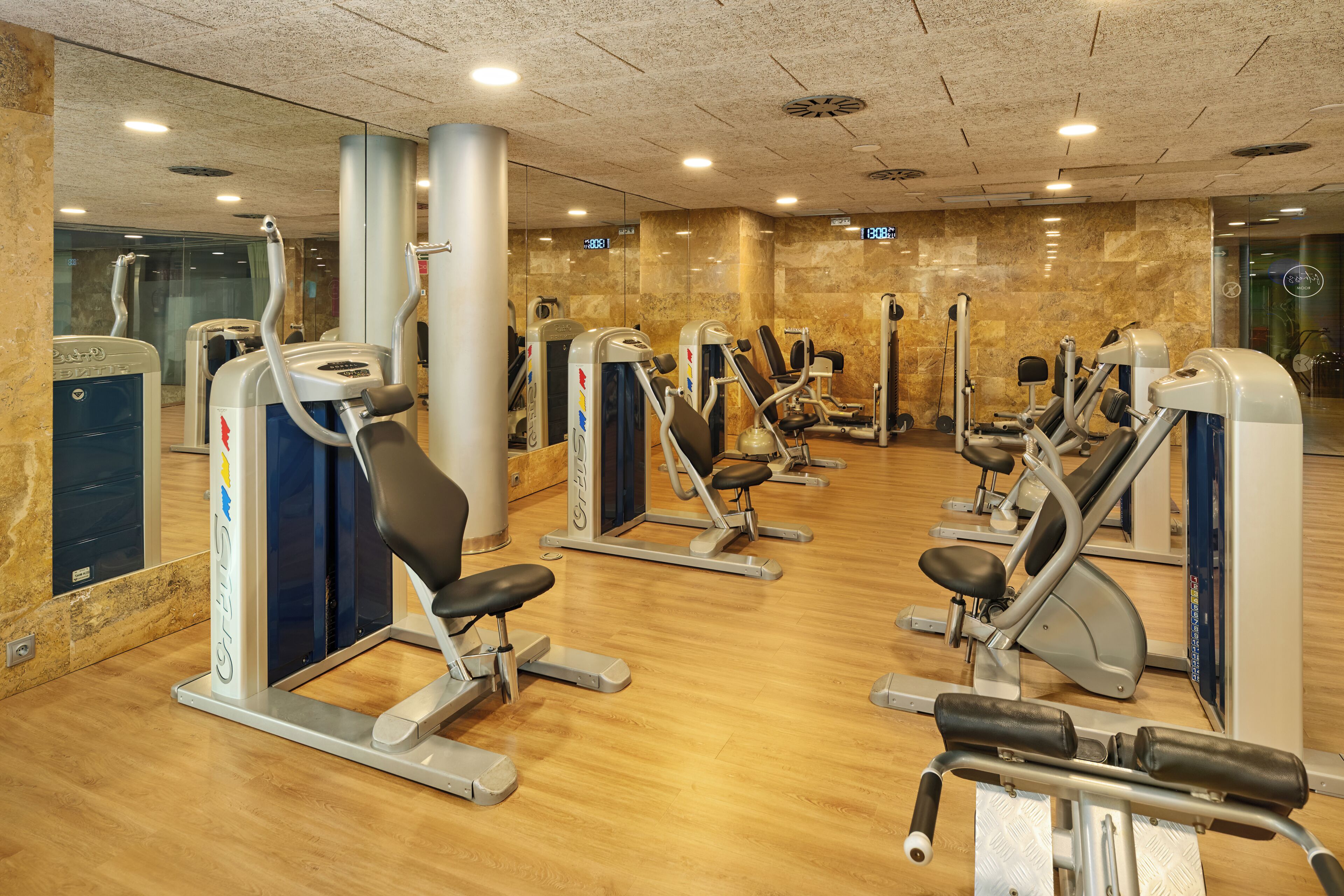 Een sportschool met diverse trainingsapparaten, een houten vloer en een marmeren wand.