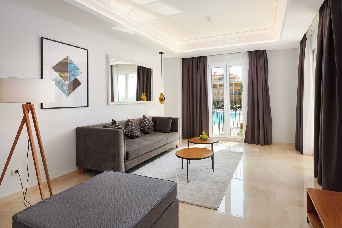 A modern living room with a sofa, a coffee table, a floor lamp, and a large window with curtains.