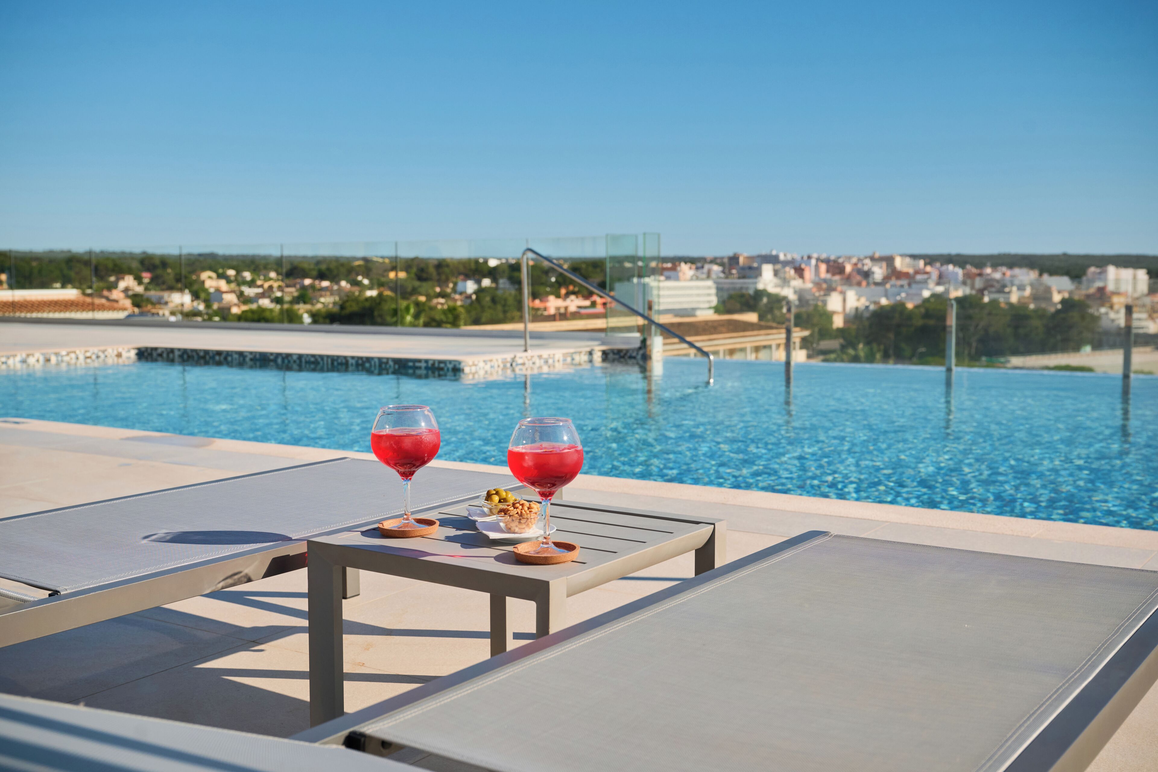 Un área junto a la piscina con sillones de descanso y una mesa con dos copas de vino tinto y un pequeño plato de aceitunas.