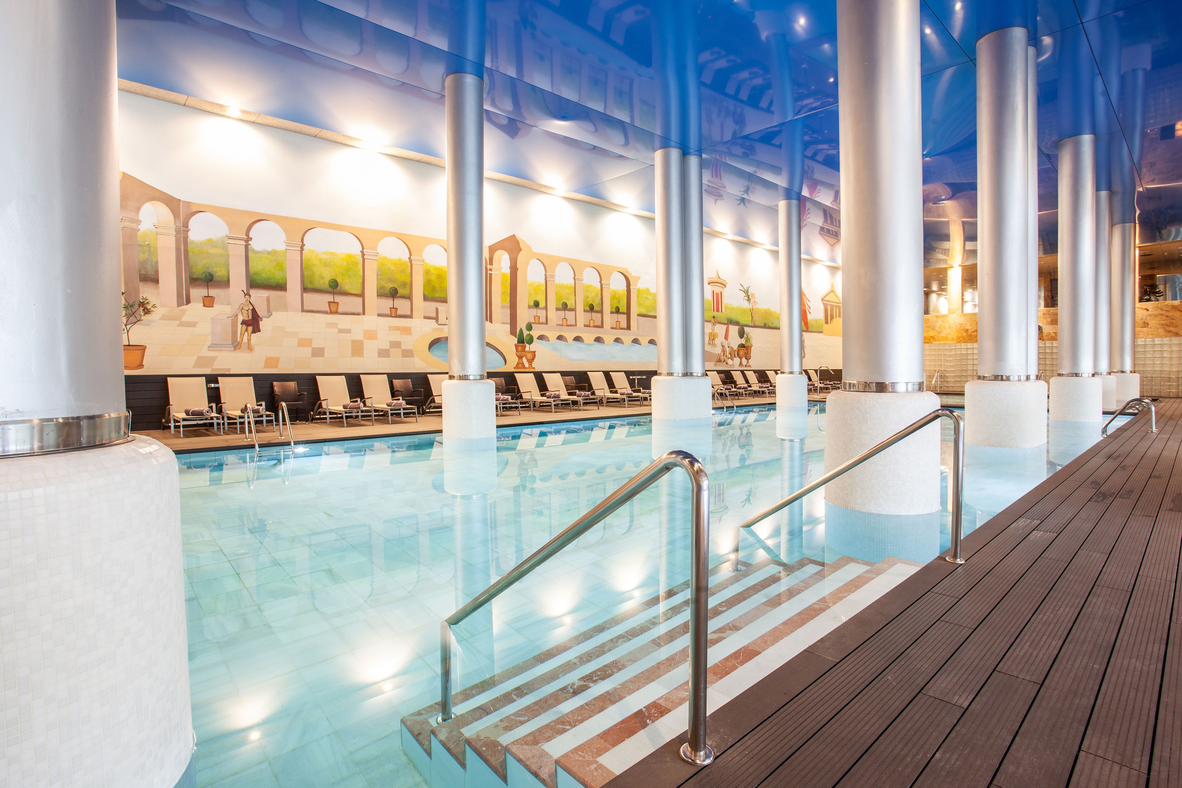 A swimming pool with a wooden deck, metal railings, and a mural on the wall.