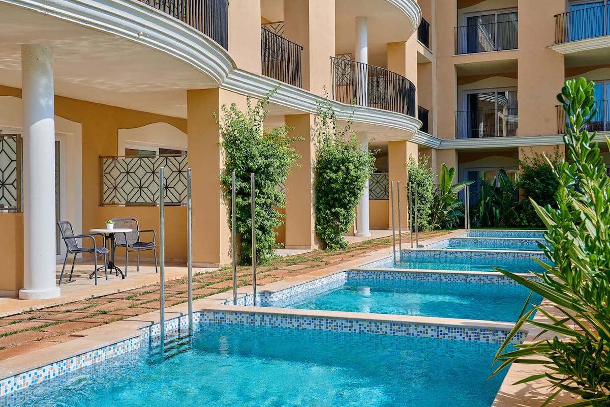 A pool area with two swimming pools, surrounded by a building with balconies and a covered seating area.