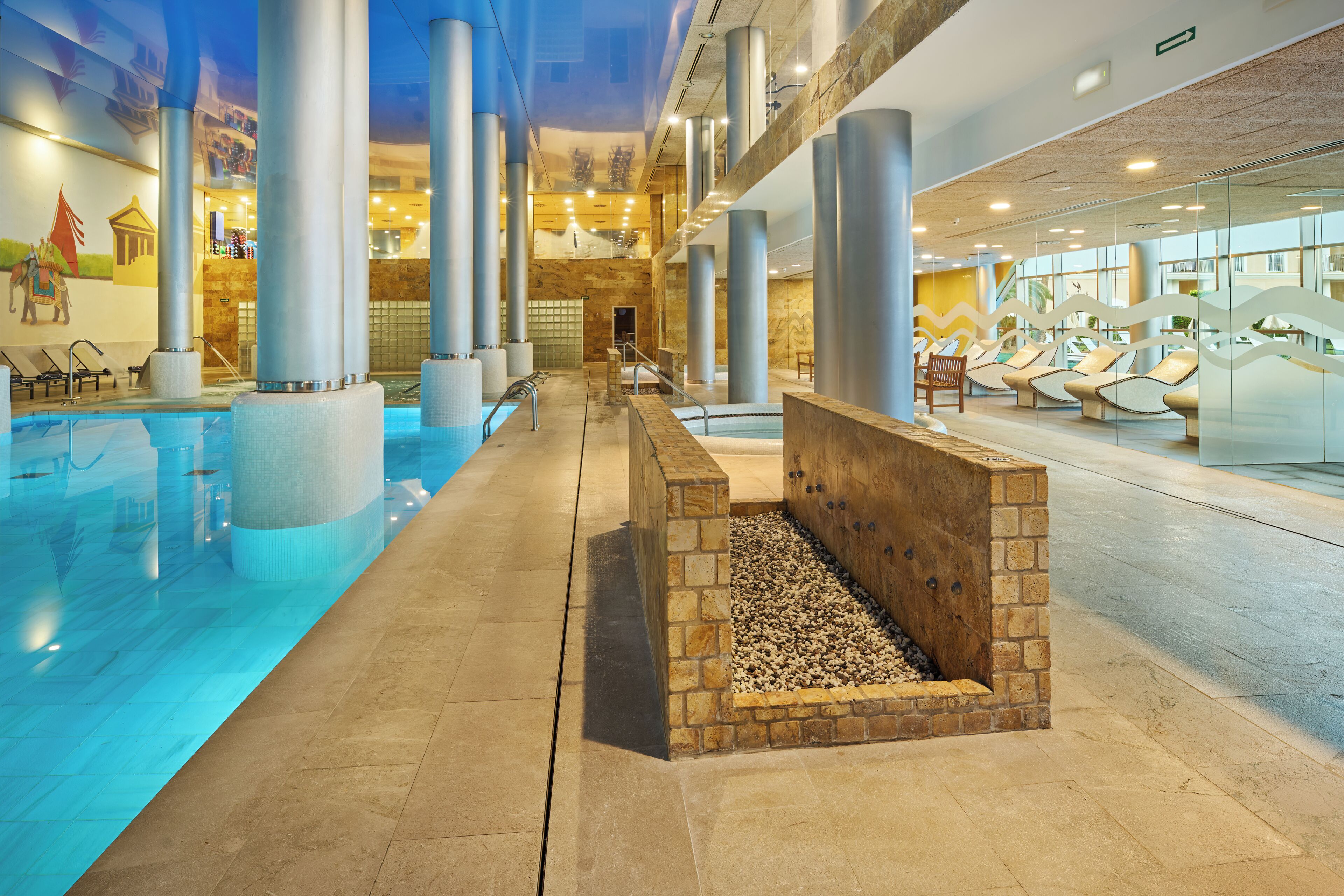 An indoor swimming pool with a stone-lined edge, lounge chairs, and a view of the interior.
