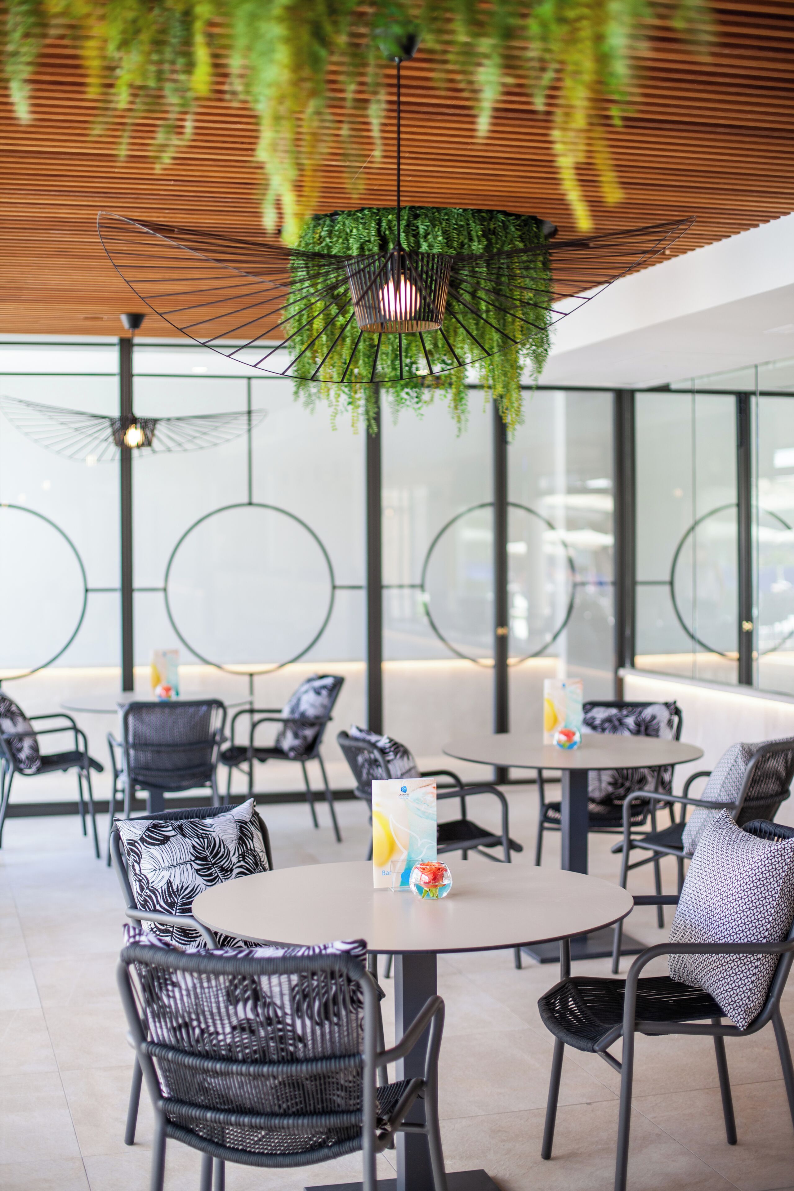 Un espace extérieur moderne, aménagé avec des tables et des chaises rondes, une plante suspendue et un plafond en bois.