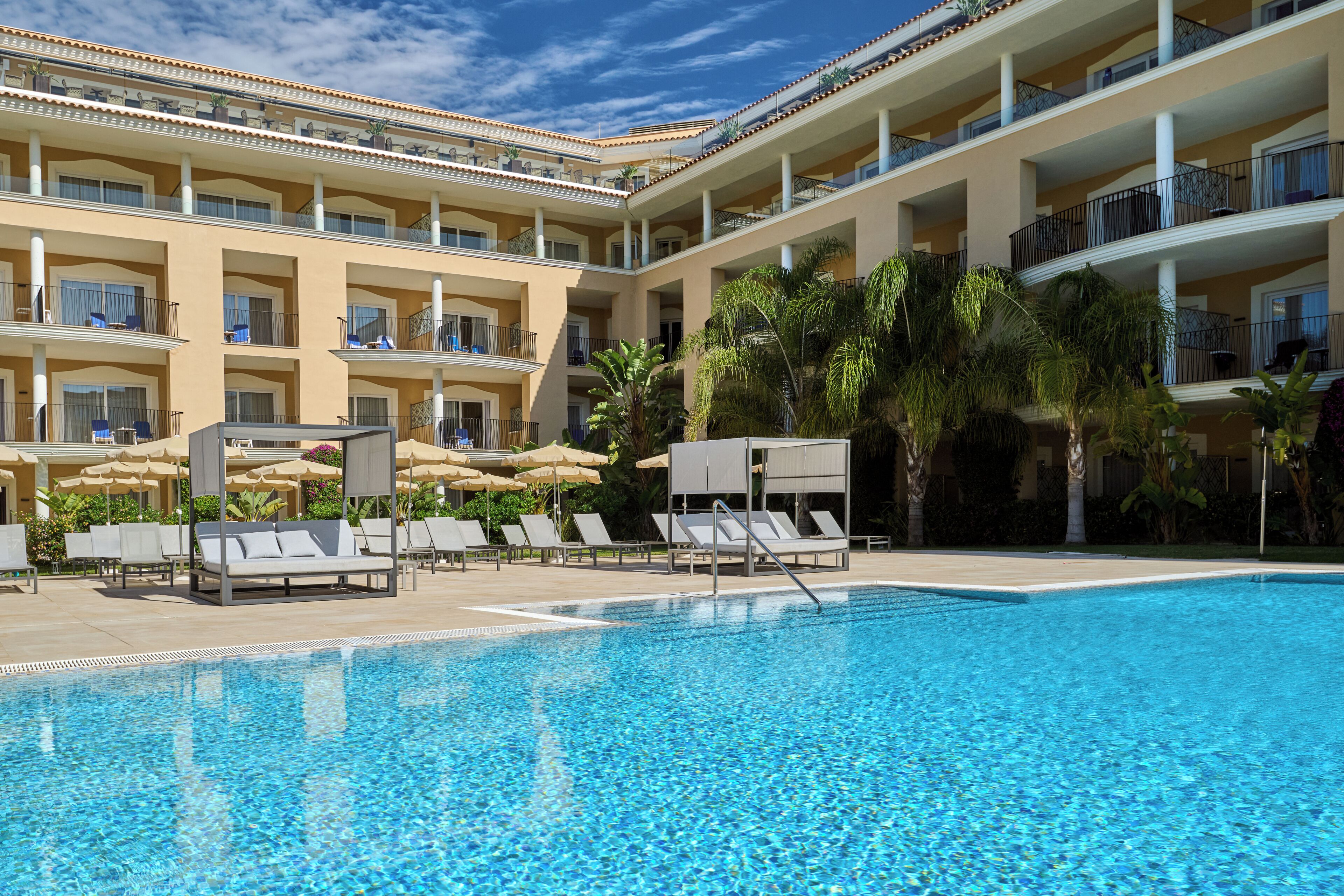 A hotel with a swimming pool, multiple balconies, and outdoor seating areas.
