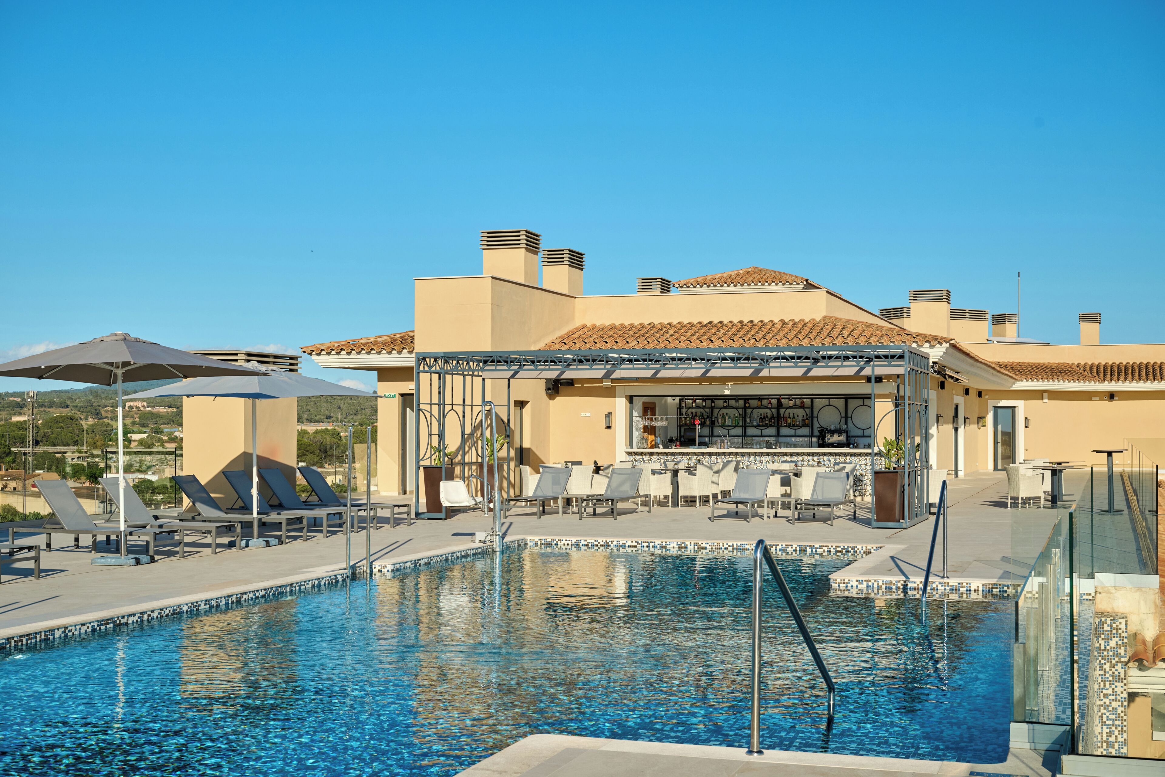Área de piscina com espreguiçadeiras, bar e céu azul.