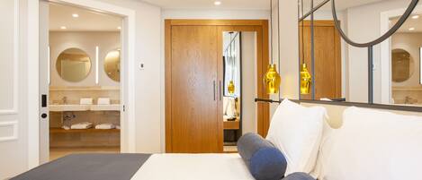 A modern bedroom with a large bed, a wooden wardrobe, and a bathroom visible through an open door.