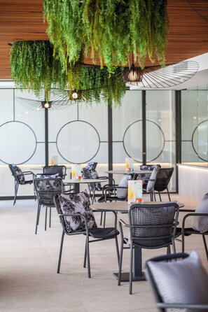 A modern dining area with round tables, black chairs, and hanging greenery.