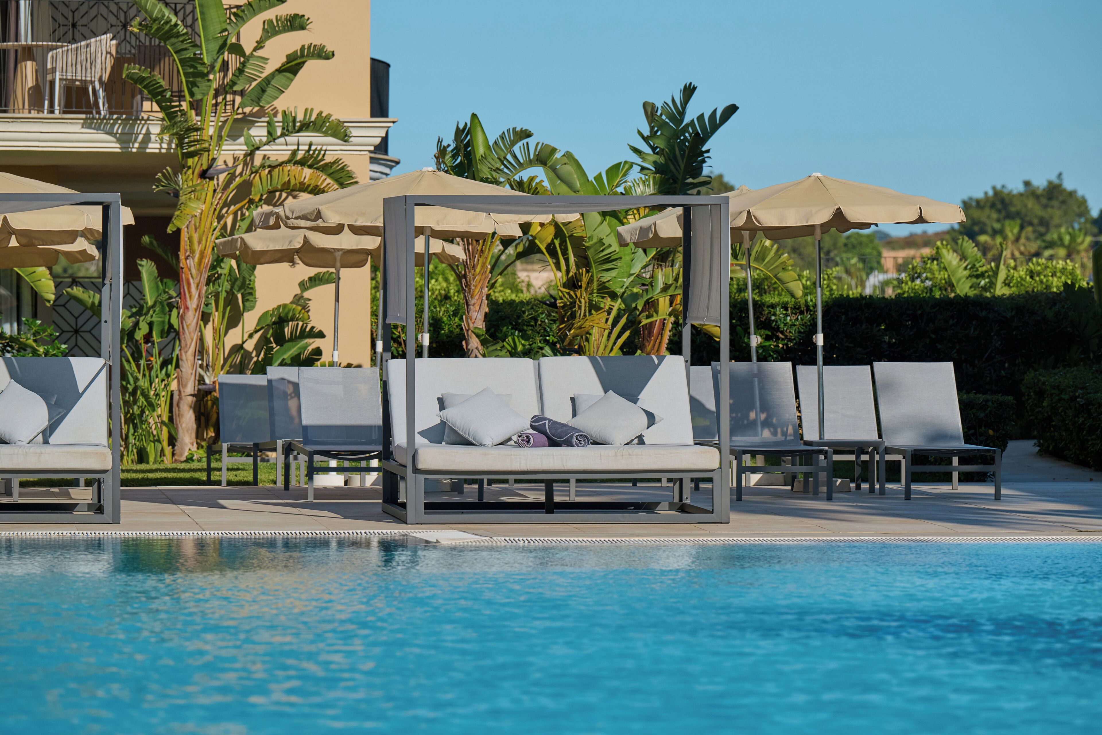 A poolside area with lounge chairs and umbrellas, surrounded by tropical plants.