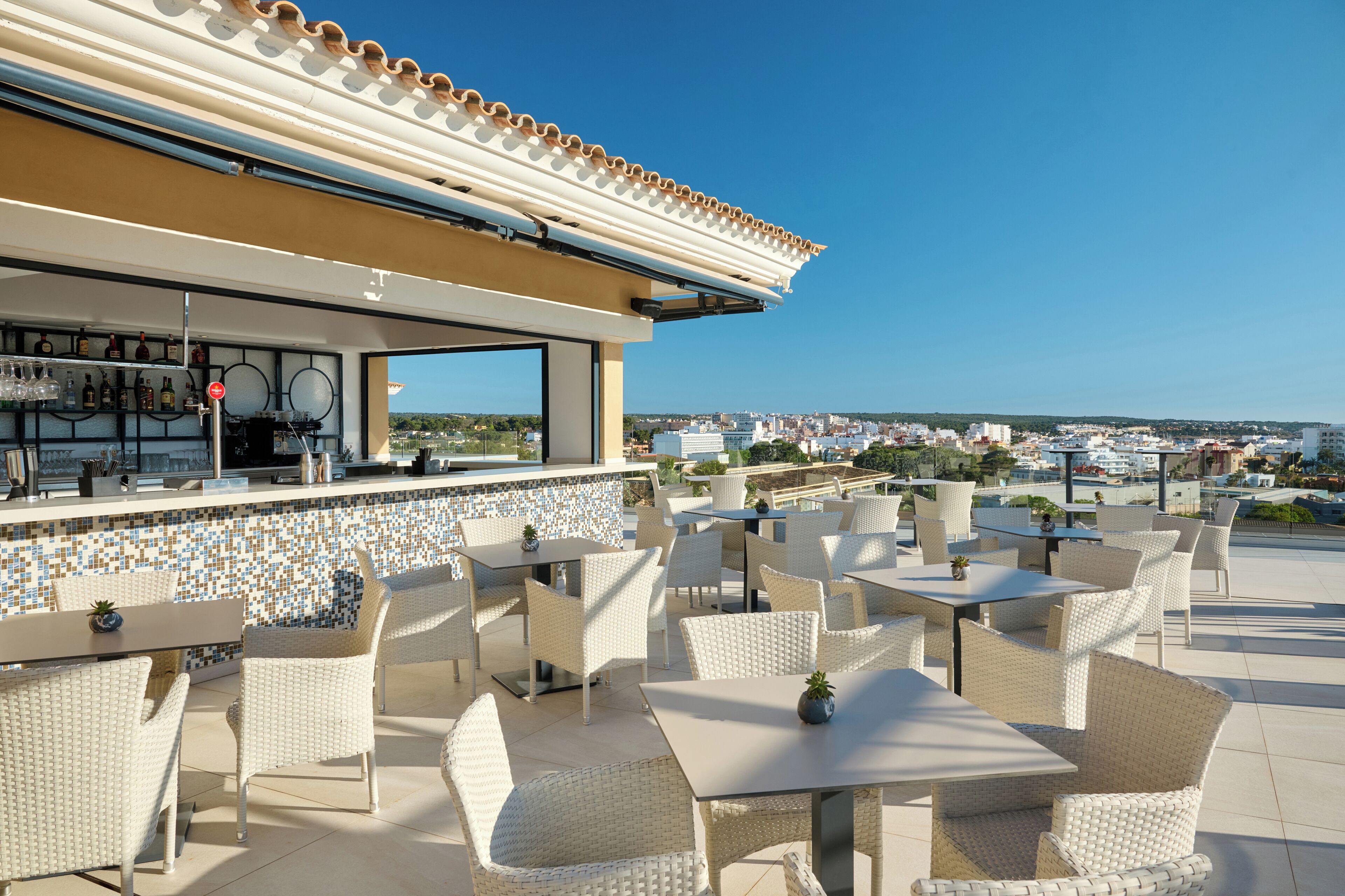 An outdoor patio with wicker furniture, a bar area with a tiled backsplash, and a view of the cityscape.