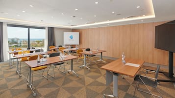 Sala de conferencias con vistas a la ciudad, equipada con mesas, sillas y una pantalla de proyector que muestra el logotipo de Grupotel.