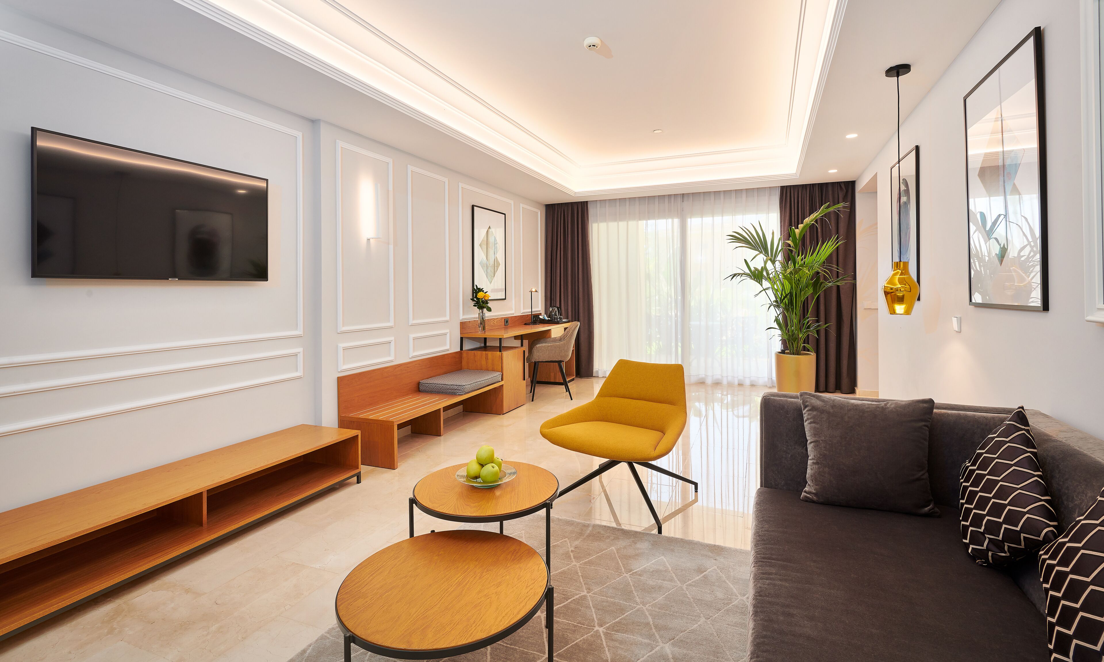 A modern living room with a flat-screen TV, a sofa, a yellow armchair, a coffee table, and a desk with a chair.