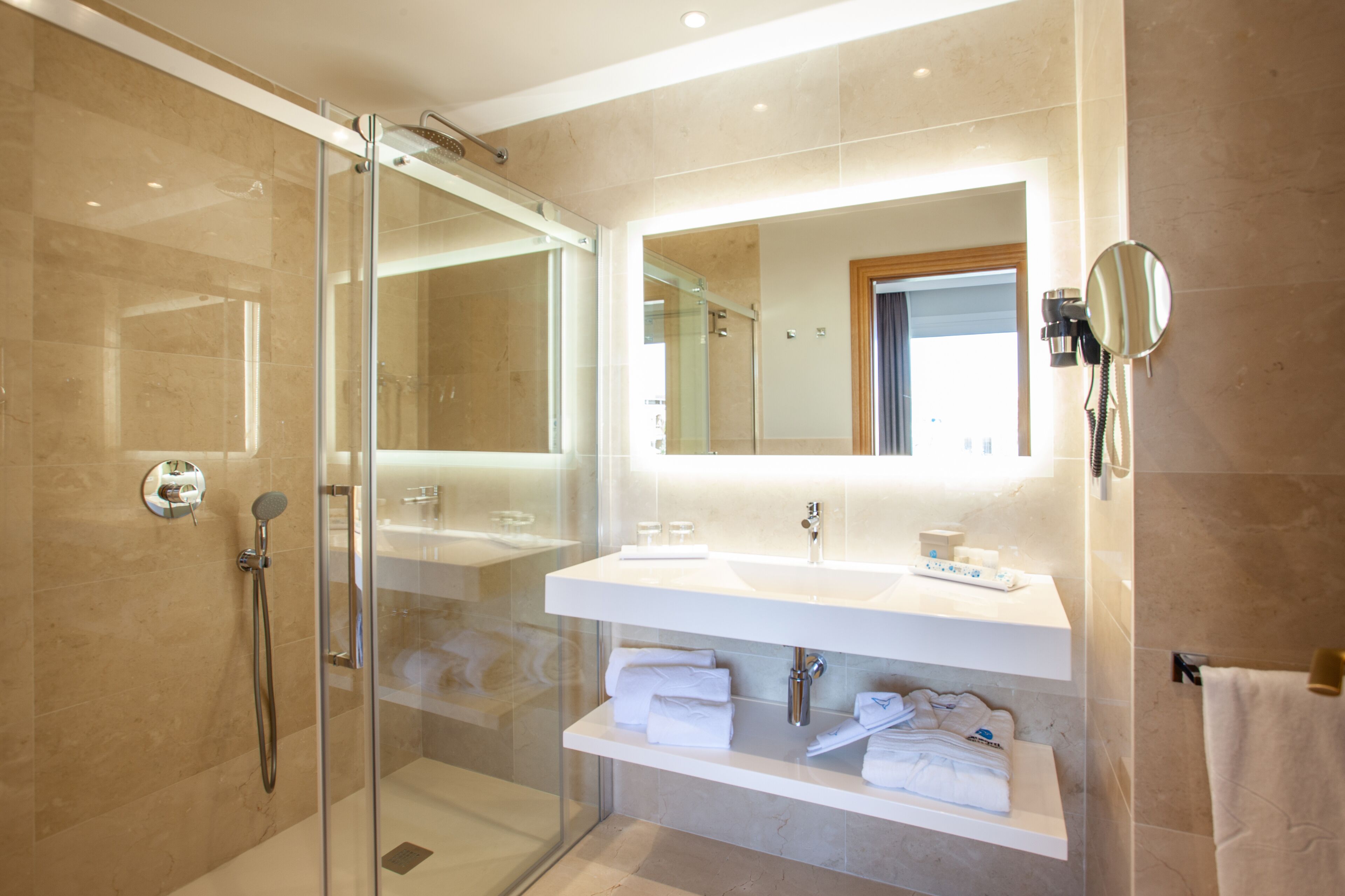 A modern bathroom with a glass-enclosed shower, a large mirror, and a white vanity with towels.