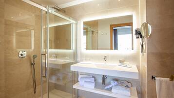 A modern bathroom with a glass-enclosed shower, a large mirror, and a white vanity with towels.