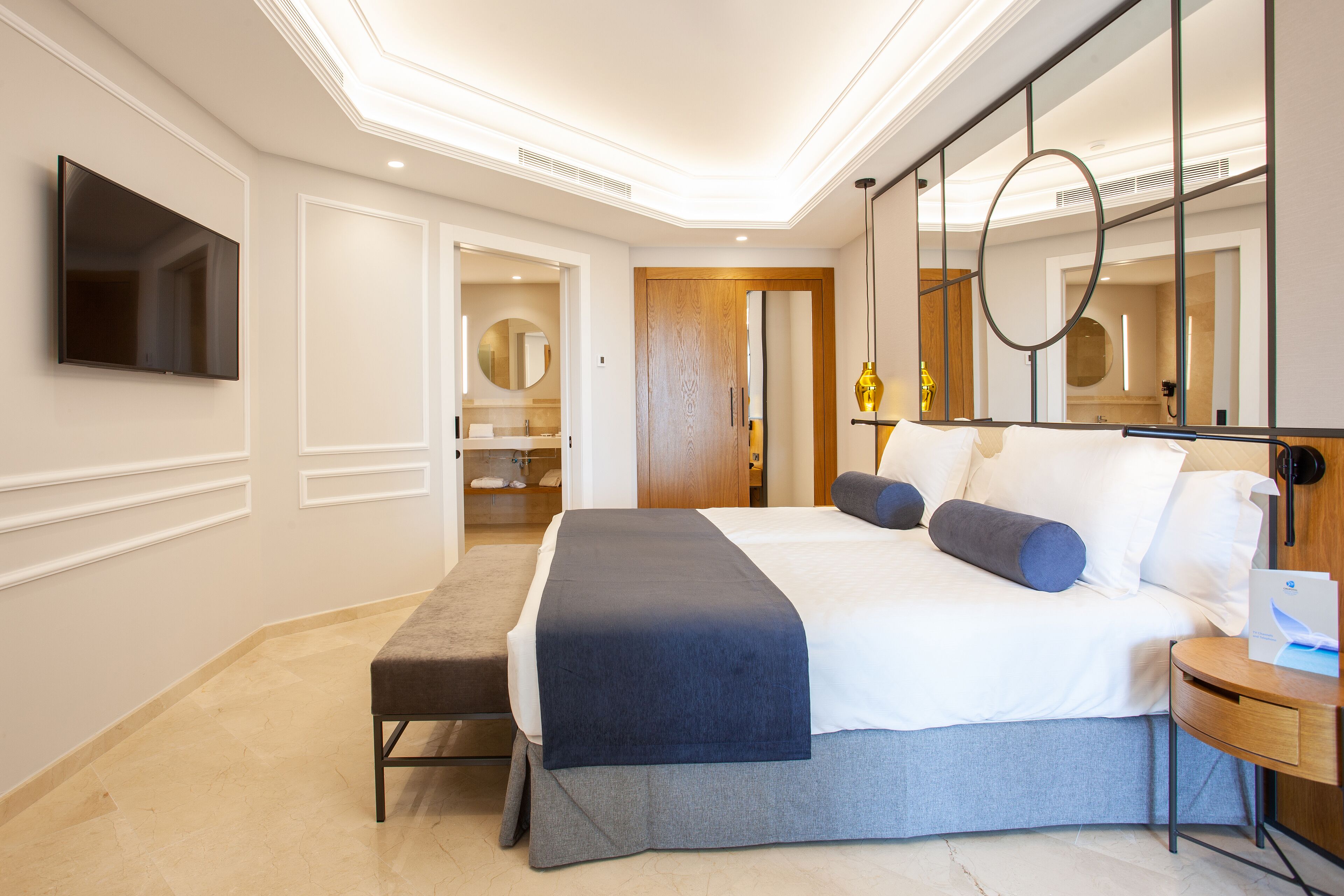 A modern hotel room with a large bed, bedside tables, a TV, and a mirror.