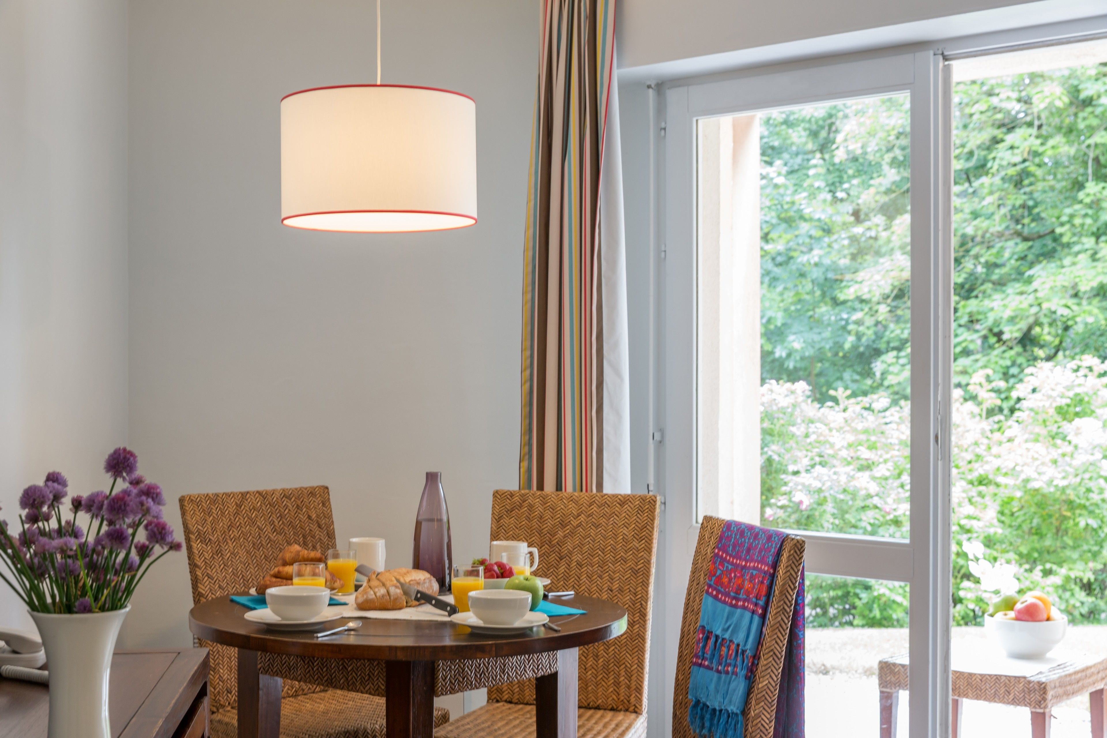 Un comedor con una mesa preparada para el desayuno, con croissants, fruta y un jarrón de flores.