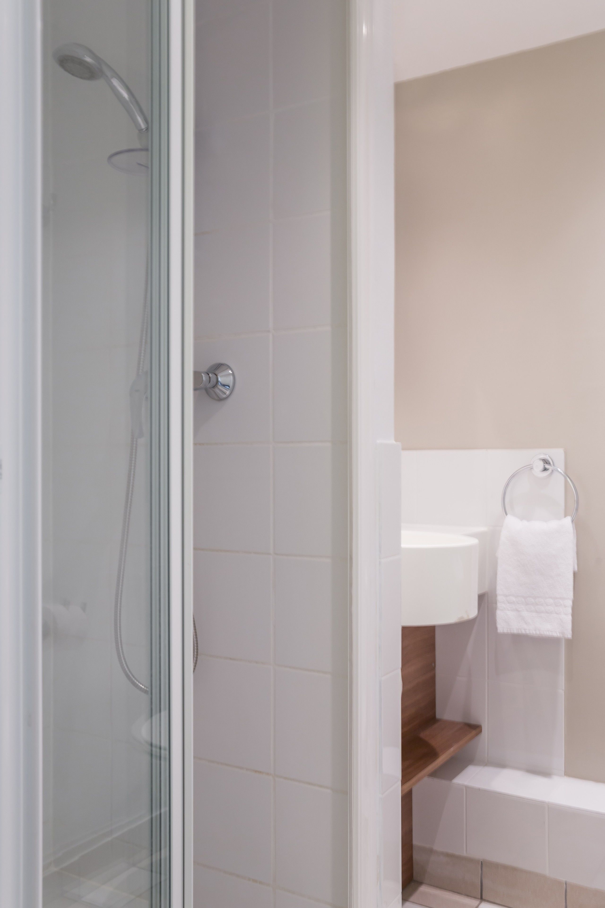 Een moderne badkamer met een douchecabine van glas, een witte wastafel en een houten plank.