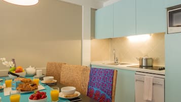 A modern kitchen with a dining table set for breakfast, including croissants, fruit, and juice.