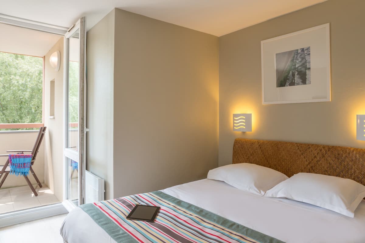 A hotel room with a bed, a window, a balcony, and a wall-mounted picture.