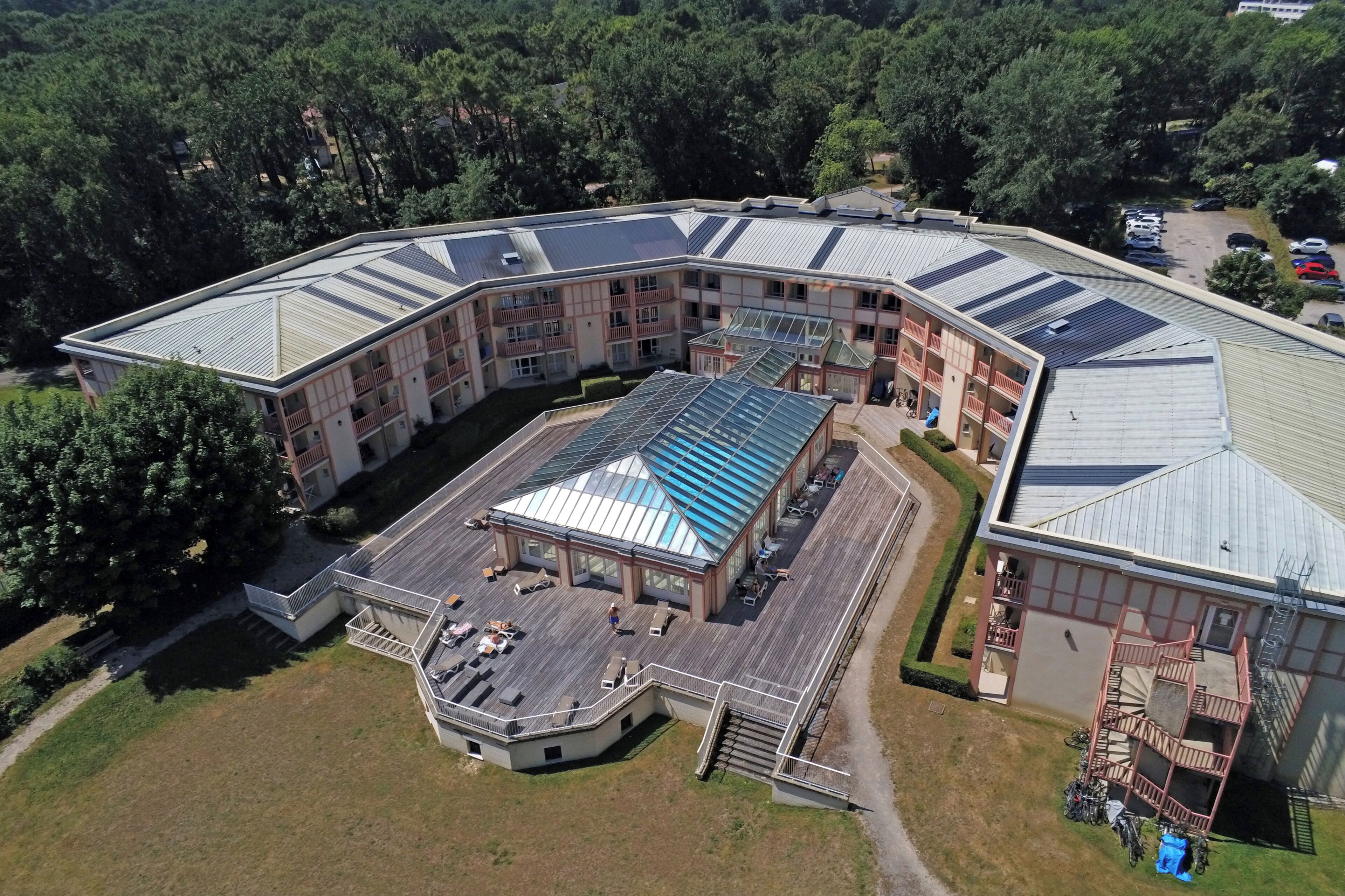 A large, multi-story building with a curved roof, surrounded by trees. It features a central courtyard with a glass roof and outdoor seating.