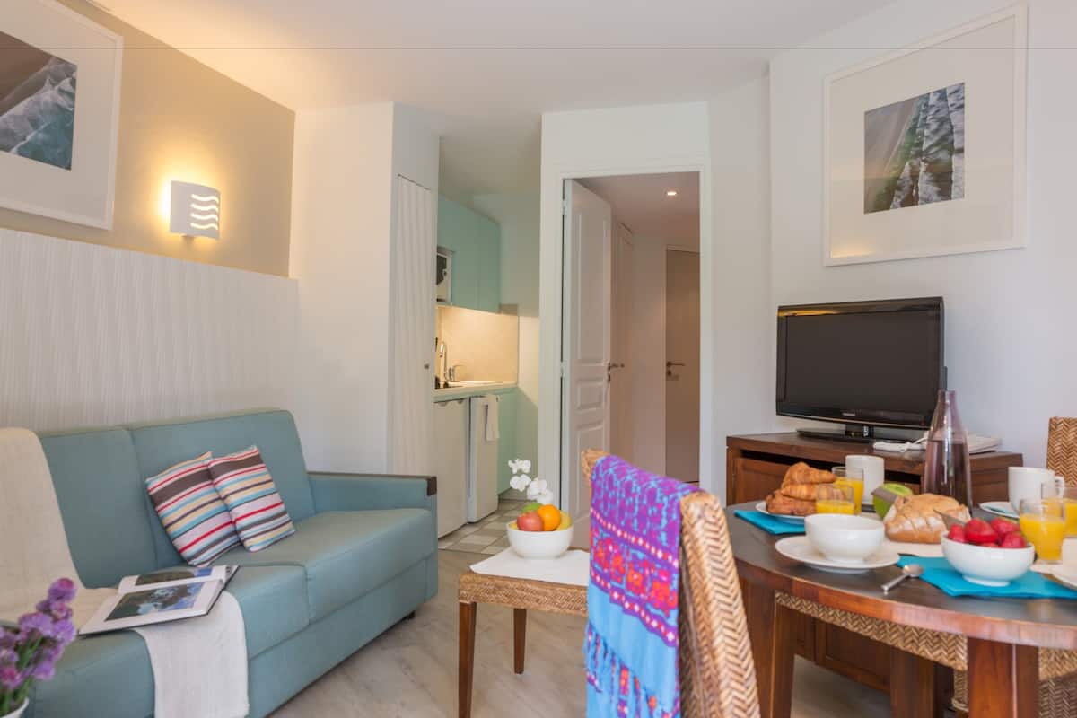 A modern living room with a sofa, a dining table set with breakfast, a TV, and a kitchen in the background.