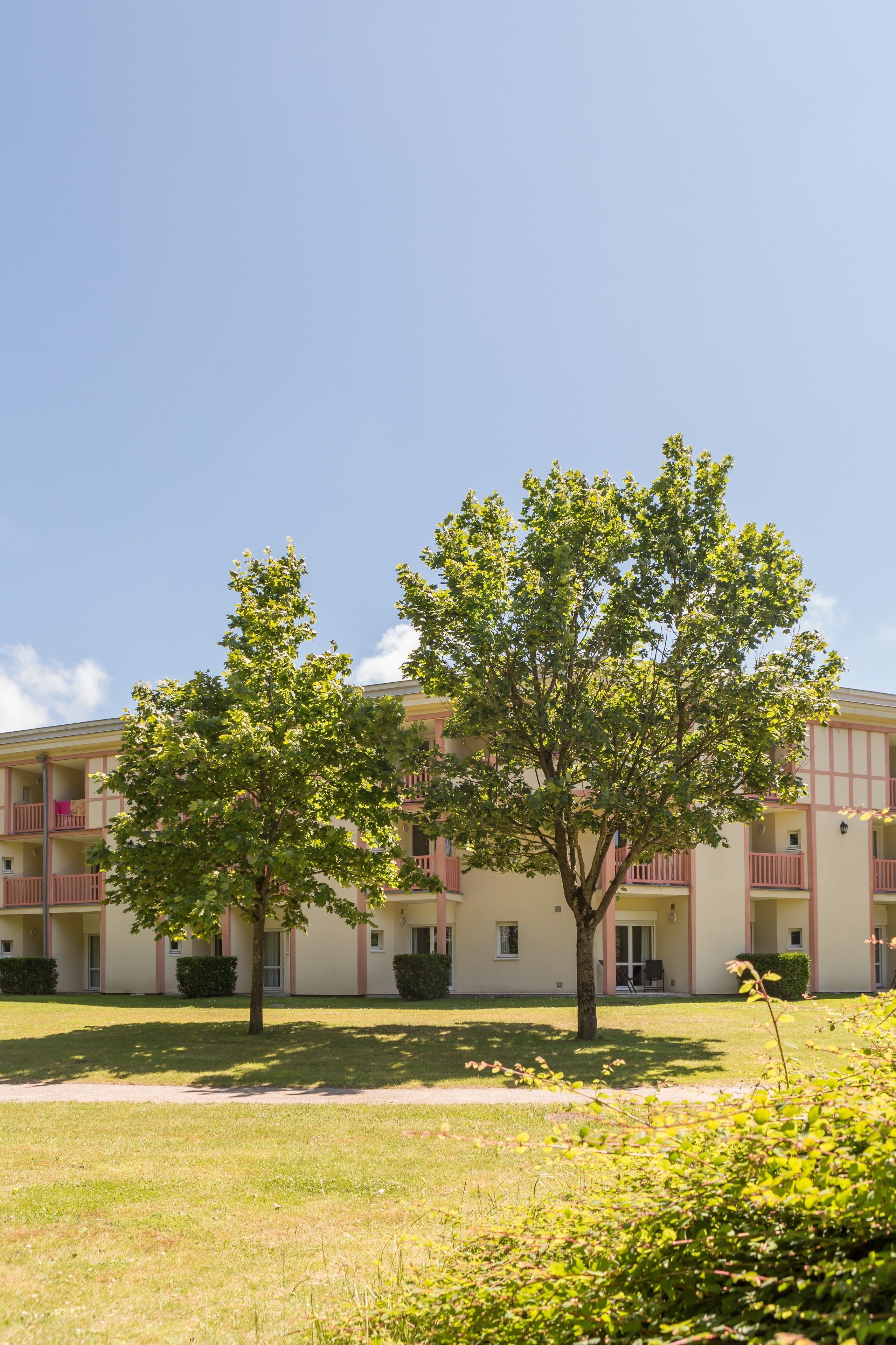 A building with a symmetrical facade, balconies, and a well-maintained lawn.