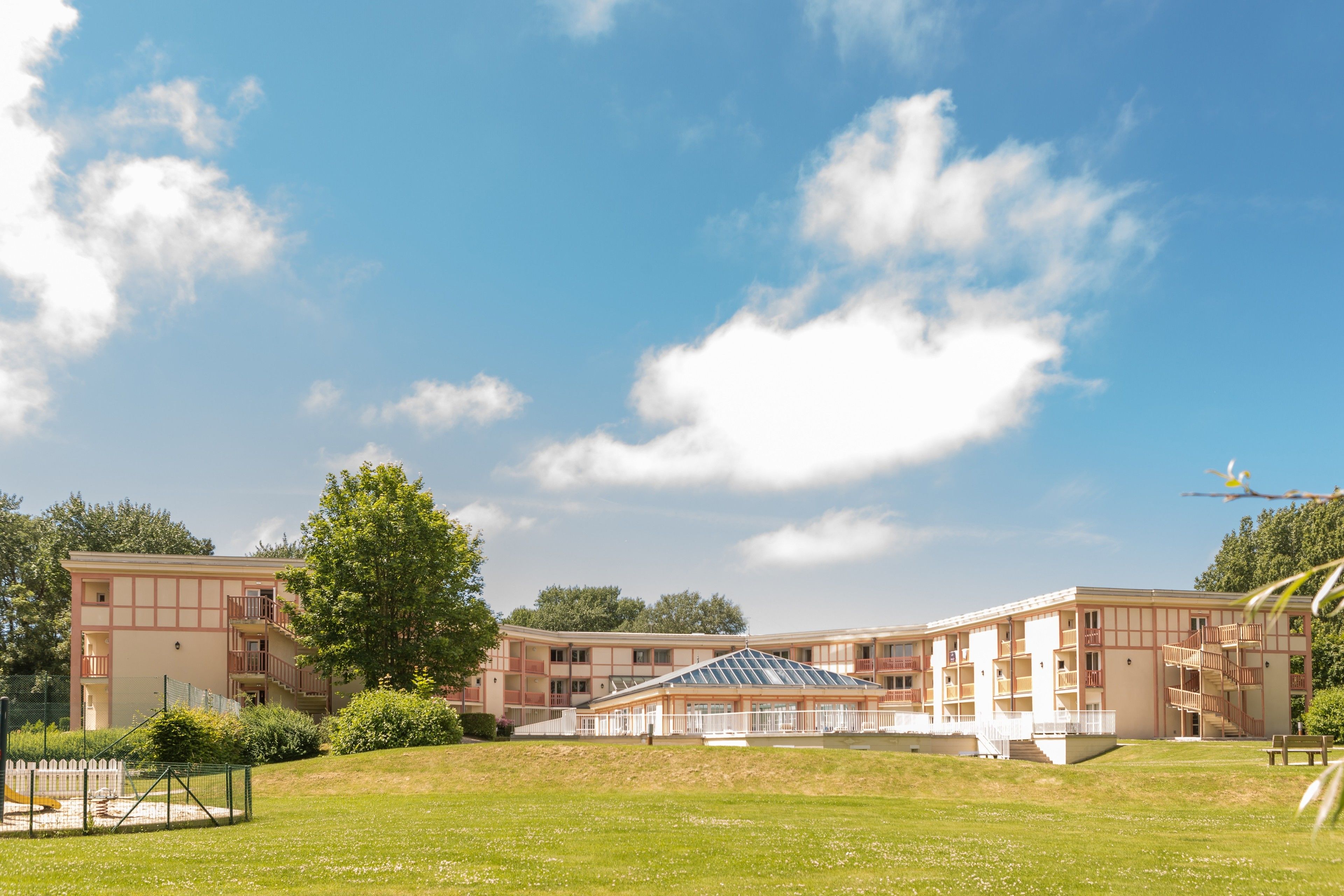 A multi-story building with a central atrium, surrounded by a grassy area and trees.