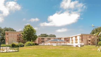 A multi-story building with a central atrium, surrounded by a grassy area and trees.