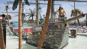 A pirate-themed water attraction with a ship structure, palm trees, and a pool area with lounge chairs.