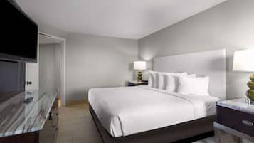 A modern hotel room with a large bed, bedside tables, a flat-screen TV, and a marble bathroom counter.