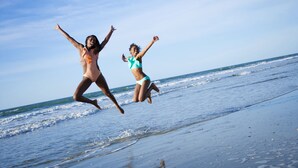 Två personer som hoppar på en strand med vågor i bakgrunden.
