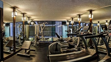 Une salle de sport équipée de divers appareils d’exercice, de miroirs et offrant une vue sur l’extérieur grâce à de grandes fenêtres.