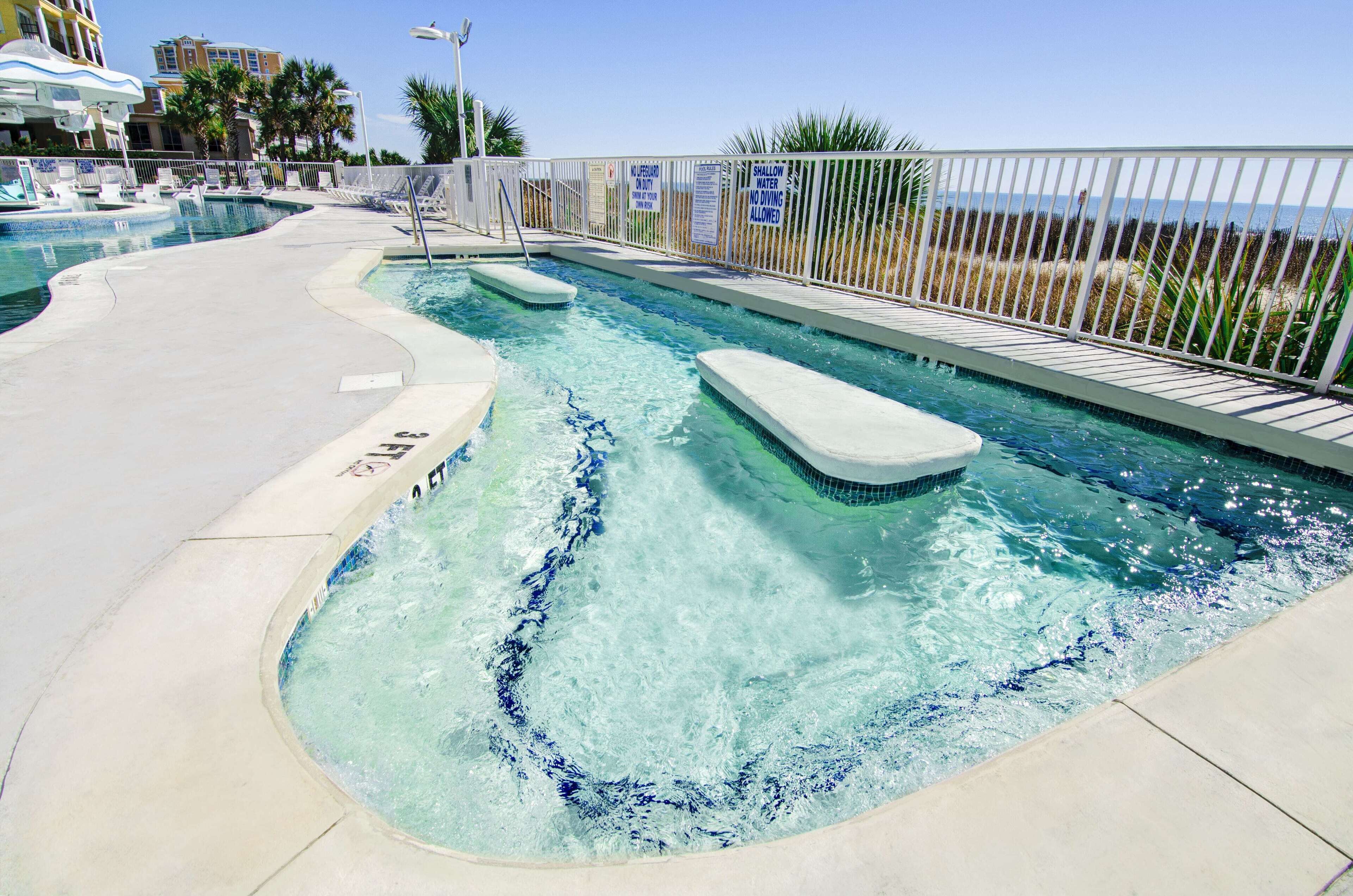 A swimming pool with a clear blue water feature, a lounge area with chairs, and a view of the ocean.