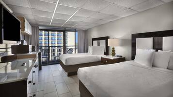 A hotel room with two beds, a desk with a lamp, a television, and a view of a building through a large window.
