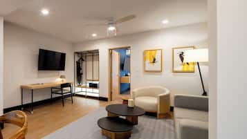 A modern living room with a flat-screen TV, a desk, a sofa, a chair, and a ceiling fan.