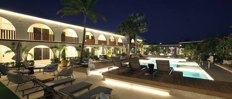A resort pool area with lounge chairs, a pool, and a building with arched windows.