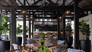 An outdoor dining area with wicker furniture, potted plants, and hanging pendant lights. - voco Surfside Aruba by IHG (Oranjestad)