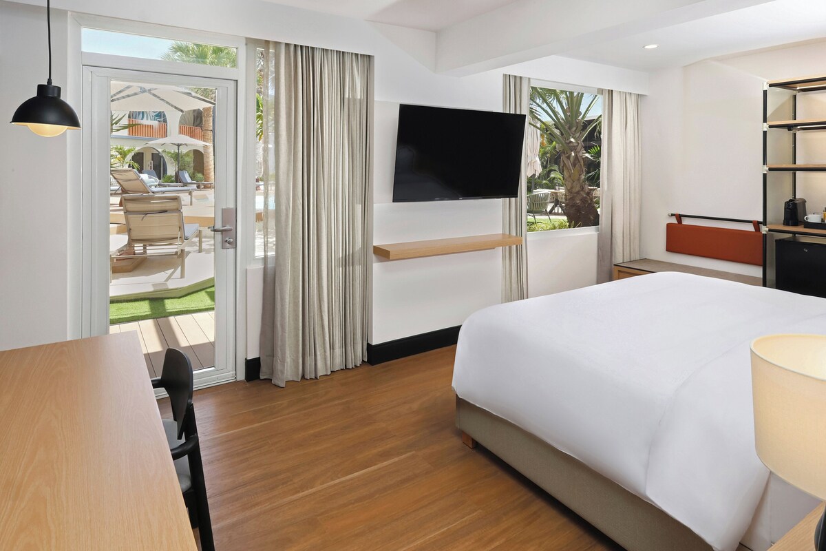 Habitación de hotel con cama, televisor montado en la pared, escritorio y silla.