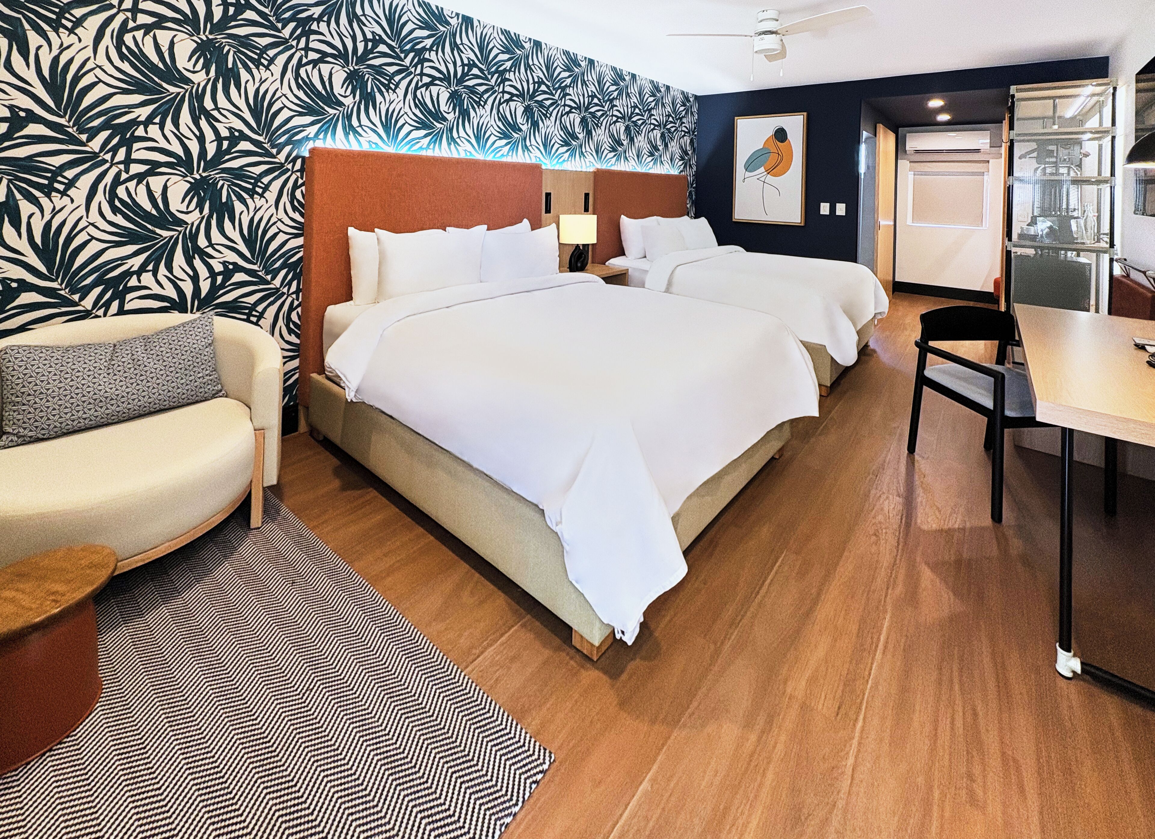 A hotel room with a large bed, a sofa, a desk, and a patterned wall.