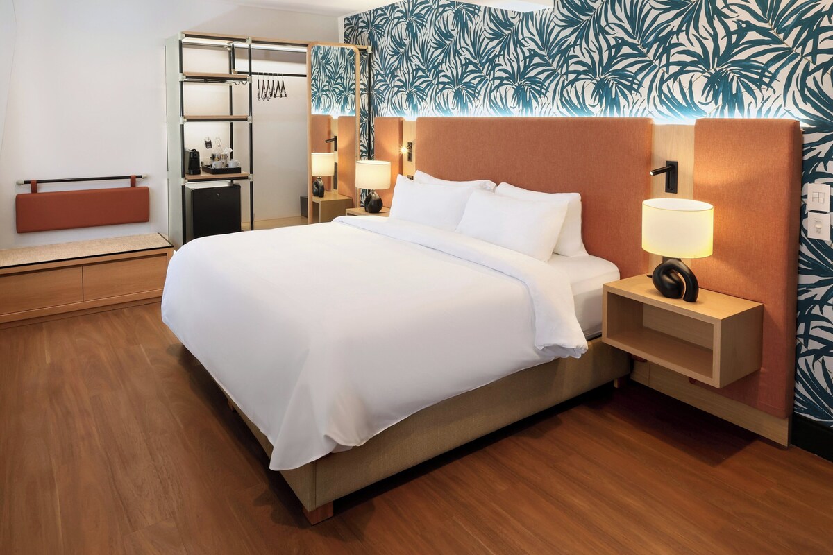Una habitación de hotel con cama, mesitas de noche, escritorio, armario y pared con diseño.