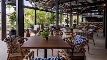 Un área de comedor al aire libre con mobiliario de mimbre, una mesa de madera y plantas en macetas.
