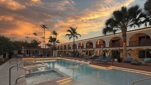 A pool area with lounge chairs, palm trees, and a building with arched windows. - voco Surfside Aruba by IHG (Oranjestad)