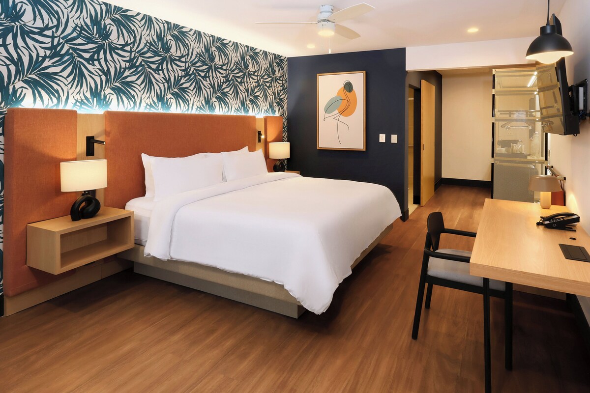 Una habitación de hotel con cama, mesitas de noche, un escritorio y una silla.