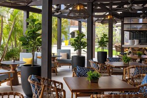 An outdoor seating area with wicker furniture, potted plants, and a view of the outdoors. - voco Surfside Aruba by IHG (Oranjestad)