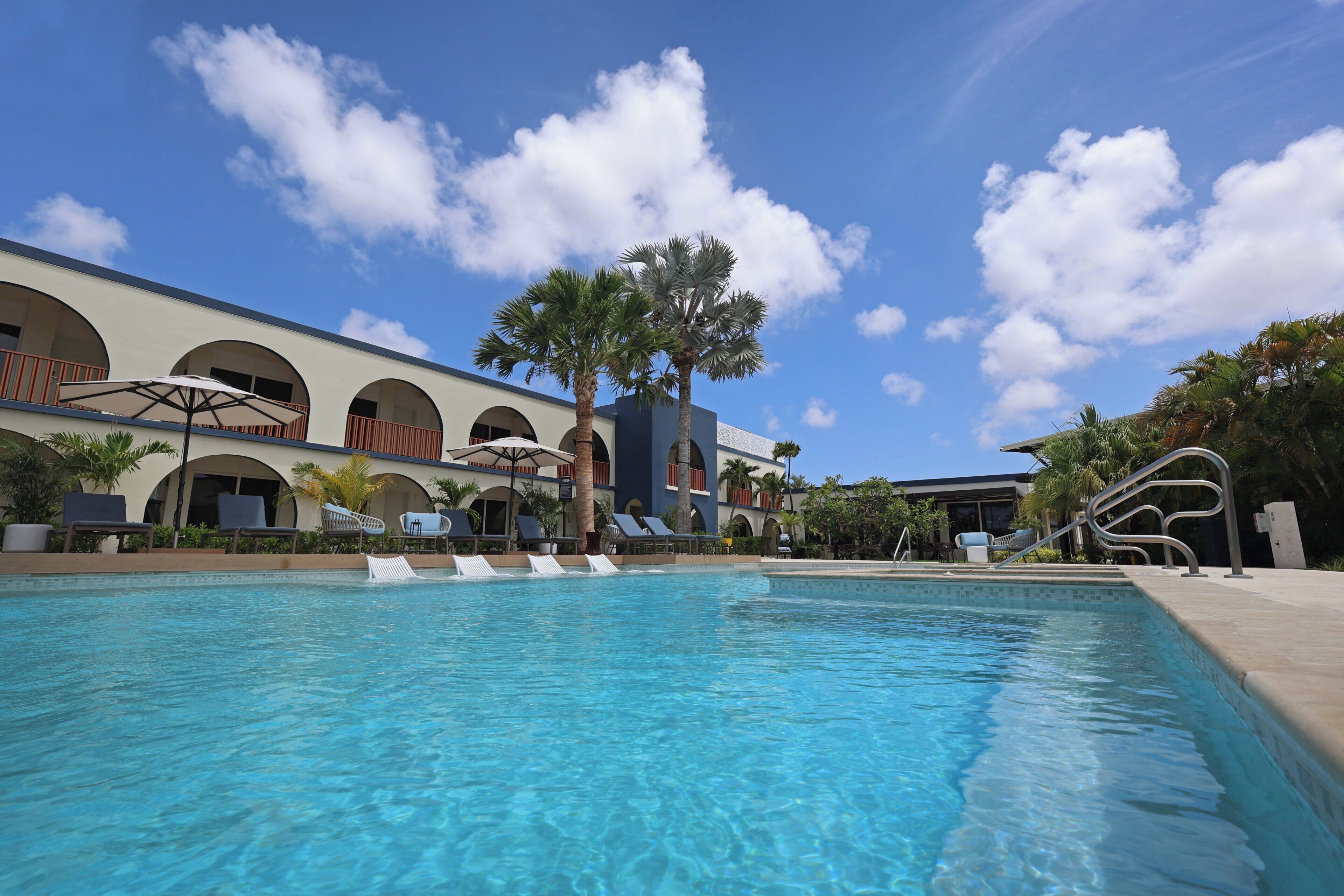 A swimming pool with lounge chairs, palm trees, and a building with arched windows.