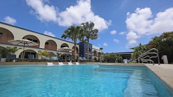 A swimming pool with lounge chairs, palm trees, and a building with arched windows.