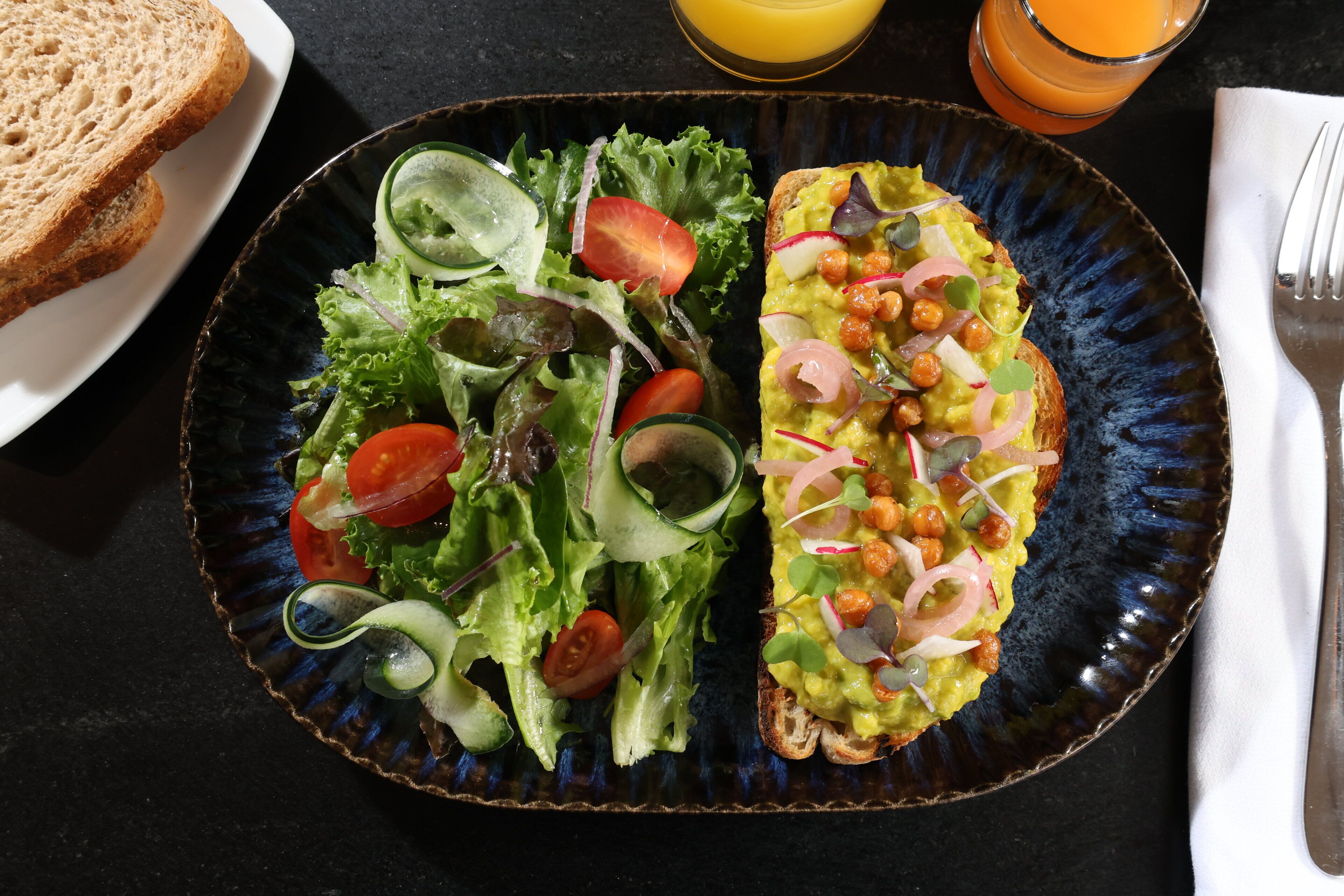 A plate with a salad and an omelette, a glass of orange juice, and a slice of bread on a table.
