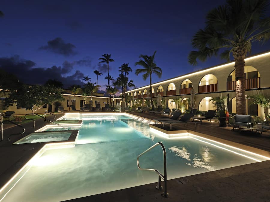 A pool area with multiple pools, lounge chairs, palm trees, and a building with arched windows.
