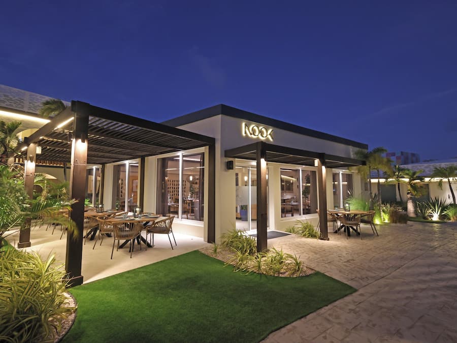A modern building with a covered outdoor dining area, palm trees, and a well-maintained lawn.